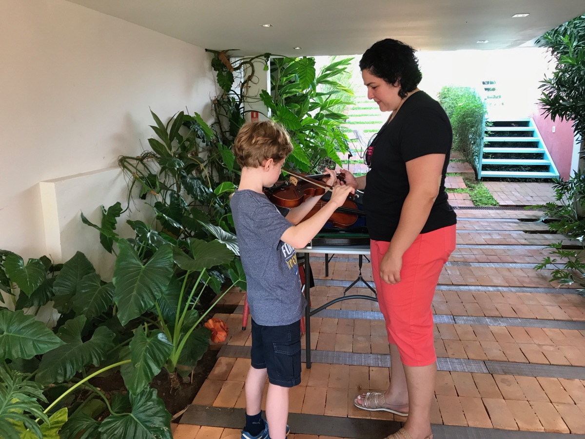 Professora orientando um aluno de violino no jardim da escola