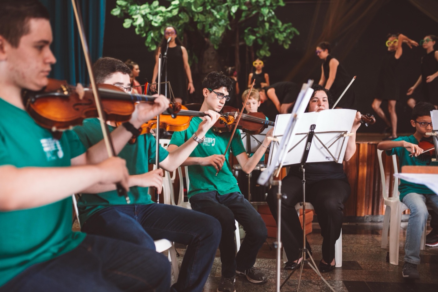 Jovens da orquestra tocando violino num palco
